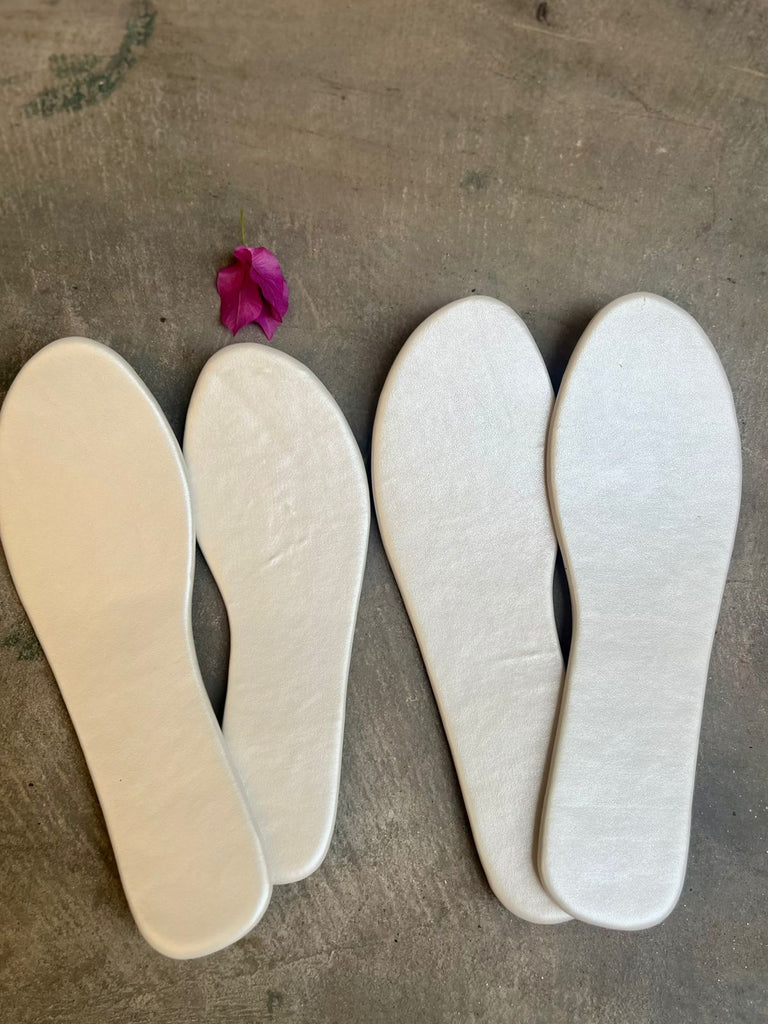 Two pairs of white shoe insoles on a textured surface with a pink flower.