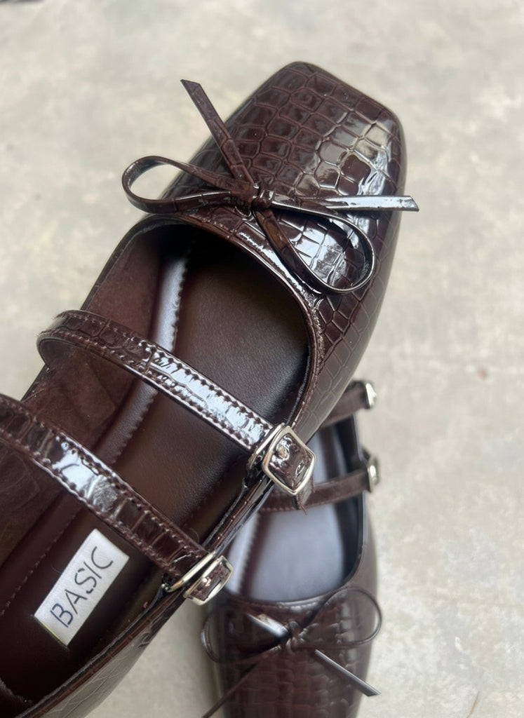 Brown patent leather shoes with decorative straps on a light background