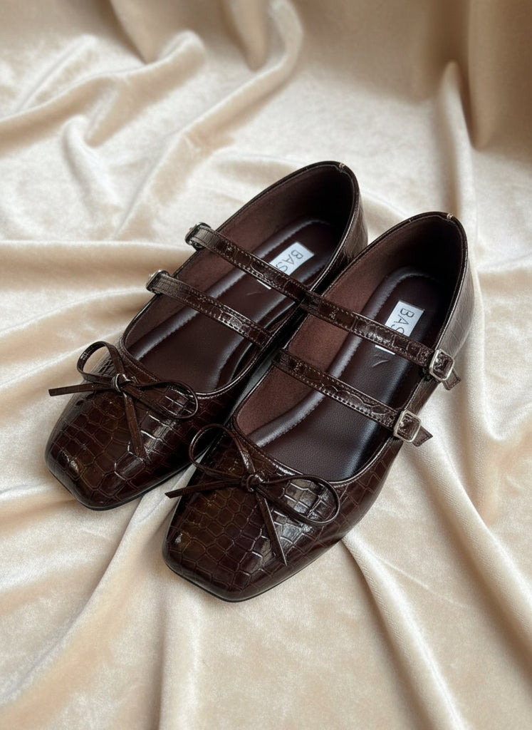 Pair of brown leather shoes with decorative straps on a gray concrete surface