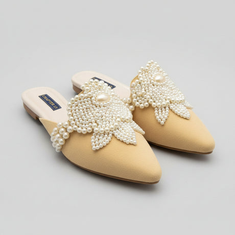 A pair of beige pointed-toe mule flats with large pearl-beaded floral embellishments across the top, displayed on a wooden surface. The insoles show the brand name 'CHAPTER 13'.