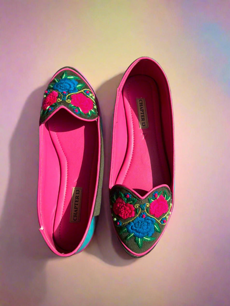 Pair of pink flats with colorful floral embroidery on a concrete surface