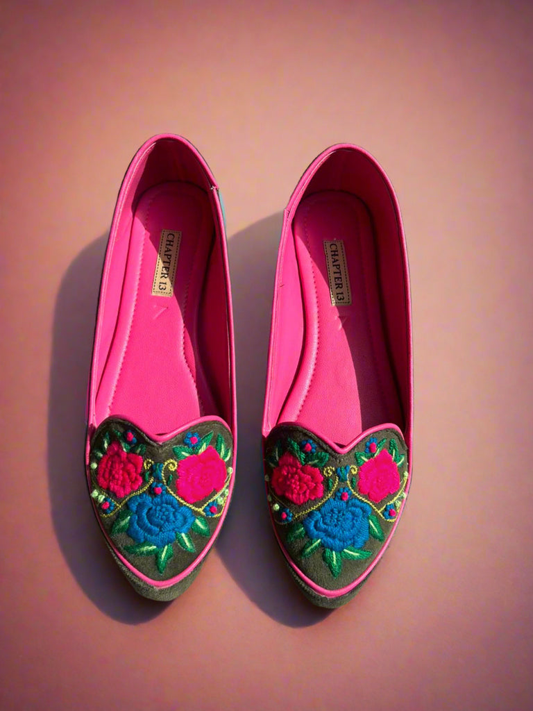 Pair of pink loafers with floral embroidery on a concrete floor
