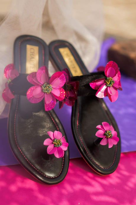 Black sandals with pink floral decorations on a pink surface