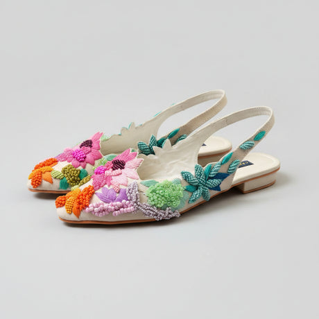 A pair of white pointed-toe slingback flats by Chaperoni, decorated with vibrant multicolored beaded floral motifs, displayed on a wooden surface.