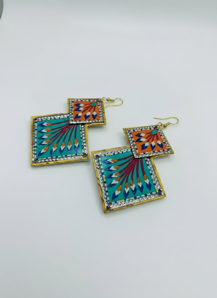 Colorful square earrings with gold accents on a wooden surface