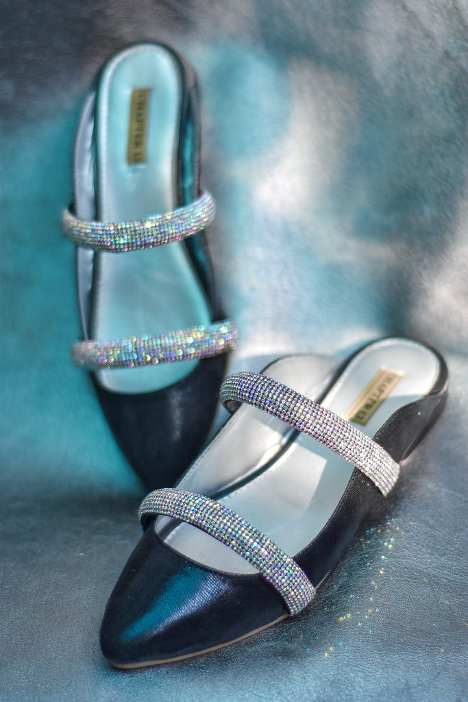 A pair of pointed bling mules with diamante straps on a blue textured background.